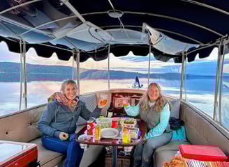 two women sitting at a table with drinks on a sunset eco-friendly electric boat cruise