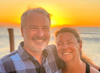 a man and woman standing in front of a sunset