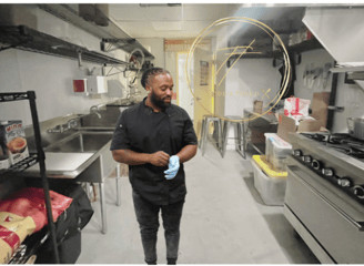 a man in a black shirt and blue jeans standing in a kitchen