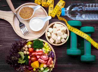 Alimentos saudáveis, fita métrica, halteres e água, representando nutrição e exercício.