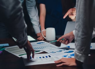 a group of people standing around a table holding papers and discussing