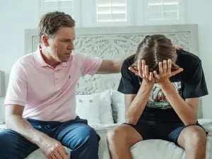 pai acolhendo o filho adolescente que chora com as mãos no rosto