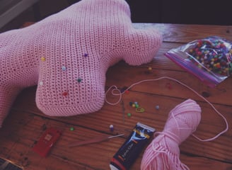 a pink crochet elephant sitting on a table with tools