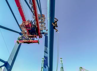Ein Höhenarbeiter seilt sich von einem Kran am Hafen ab.