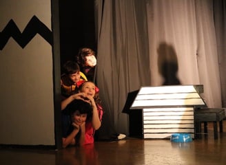 Young children performing a musical on stage in colorful costumes.