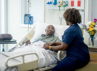 A nurse converses with an elderly man resting in a hospital bed, providing care and support during h