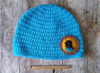 a crochet hat with a crochet hook and a felt applique with crochet edging