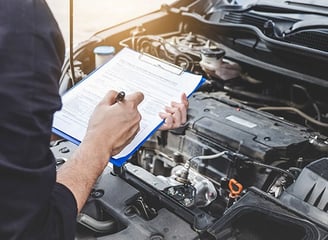 a man in a blue shirt is holding a clipboard and a clipboard evaluating a car's engine.