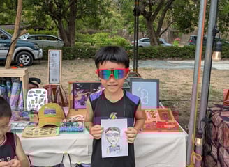 一個男孩拿著 廢材fadechai插畫家幫他速寫的人像畫，站在攤位面前