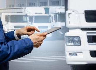 Logistics worker using tablet in front of white freight trucks — pilot delivery program coordination
