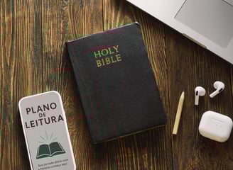 Bíblia com capa Holy Bible ao lado de plano de leitura, fones de ouvido e lápis sobre madeira