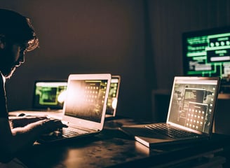 a man sitting at a desk with two laptops
