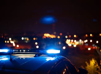 Policijos automobilio švyturėliai apšviečia naktinį miestą, simbolizuojantys saugumą ir reagavimą