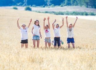 cinco niñas saltando en un campo de trigo