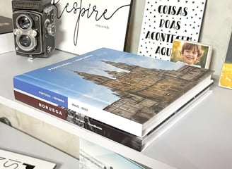 Dois Fotolivros, um sendo da Noruega e ouro de Portual e Espanha. Eles estão sobre uma mesa bem decorada com fotos.