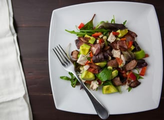 Vista cenital de un plato de carne con verduras, servida en un plato blanco, con tenedor