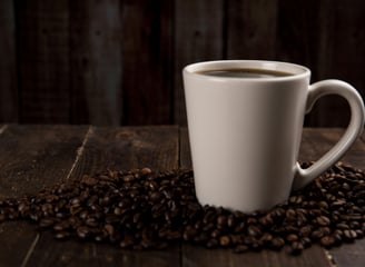 Vista lateral de una taza de café, sobre granos de café en una mesa