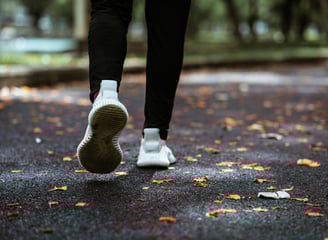 Vista trasera de una persona corriendo, vestida con ropa negra y tenis blancos