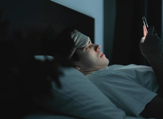 Persona acostada en su cama, revisando su teléfono celular, antes de dormir