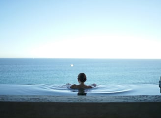 Eine Frau die in einem Infinity Pool auf das Meer schaut