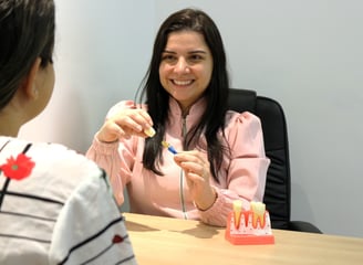 a woman in a pink shirt is sitting at a table with a dental implant on her hands