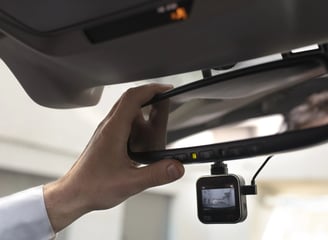 Dashcam debajo de un espejo retrovisor y la mano de un hombre acomodandola