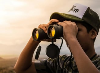 niño con gorra usando prismáticos para ver el paisaje