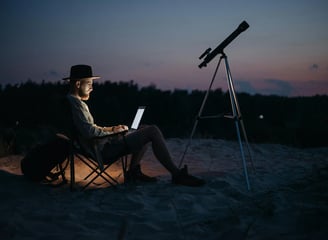 hombre sentado en una silla con una laptop y un telescopio