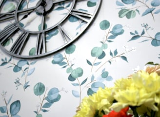 eucalyptus wallpaper with partial silver clock face with yellow flowers below