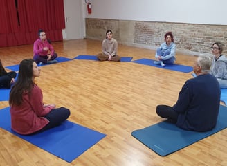 a group of people sitting on yoga mats in a circle, classe di esercizi di bioenergetica