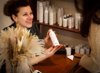 Eine Frau lächelt und hält eine Flasche Haarpflegeprodukte für Haarverlängerungen. Tressen, Bondings