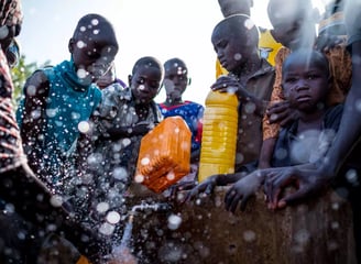 A group of African children and adults gathered around a water source, learning about hygiene