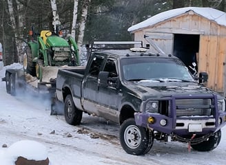 A tractor loaded on a flatbed trailer being pulled in the snow showing expertise at hauling