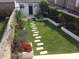 Jardin paysager avec gazon, massifs fleuris et pas japonais menant à une entrée de maison