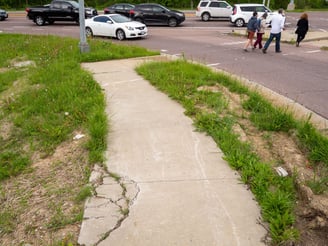 Photo of a cracked up sidewalk leading to a busy intersection