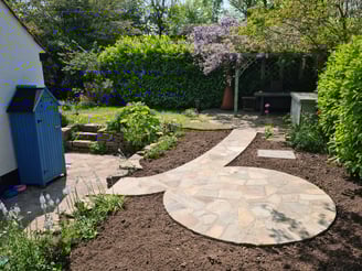 Sweeping pathway and circular patio made from old York stone in a crazy paving style.