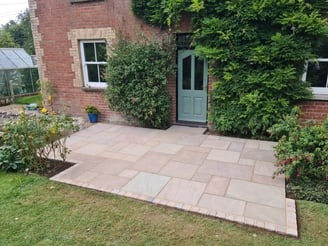 Sandstone patio laid with four different sized slabs in a random pattern, with a cobble sett edge.