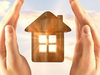 hands holding a house with a wooden house in the background