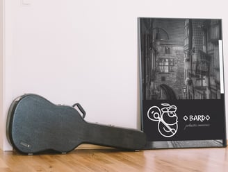 Poster em quadro com logo branco de produtora musical com homem barbudo ao lado de case de violão