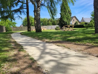 Allée en sable stabilisé sinuant à travers un jardin paysager arboré avec mobilier extérieur