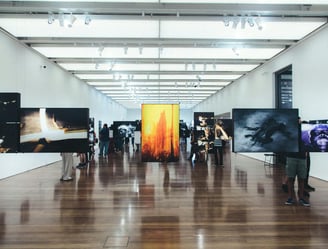 Pessoa admirando uma pintura em uma galeria de arte com iluminação suave e obras em exibição ao fund