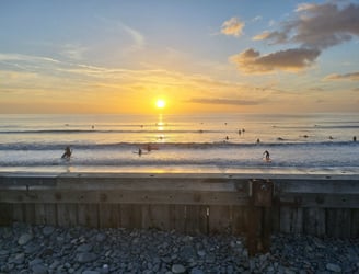 An amazing orange sun setting into the sea while. abusy after school club surf lesson goes on.