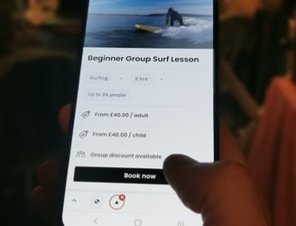 A mobile phone displaying a beginner group lesson booking page, a thumb about to click book now