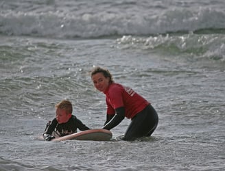 A young surfer with a female surf coach holding the board waiting for a wave