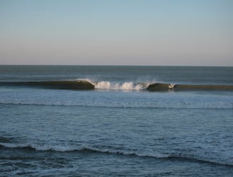 A large A frame peak, with a surfer taking off on the wave peeling to his left.