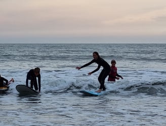 Two surfers on the same wave one standing the other getting to their feet.