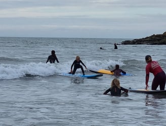 A busy after school surf club lesson with a young male surfer an a wave other children watching