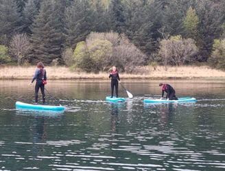 2 paddle board students and SUP coach on a calm lake.