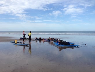 Two surf coaches delivering a surf safety brief to a large group on the beach