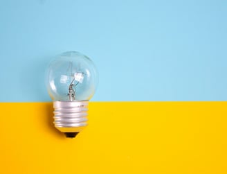 A clear lightbulb against a split blue and yellow background, representing new ideas, creativity, an